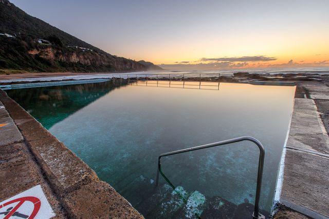 Sunrise casting a warm glow over a serene ocean pool beside a cliffside beach. Tranquil reflections on calm water creating a peaceful and relaxing atmosphere. Perfect for travel brochures, nature blogs, holiday destination promotions, and relaxation-themed projects.
