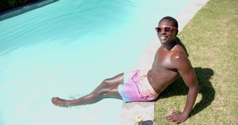 Smiling man relaxing poolside on sunny day in vibrant shorts