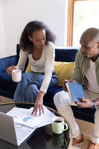 Diverse couple planning household budget at home, reviewing charts and laptop together