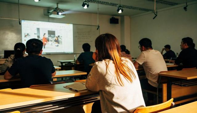 Female student watching projected lecture and taking notes in university classroom