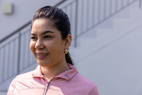 Smiling woman in 30s wearing pink zip-up activewear and gold hoops near urban staircase