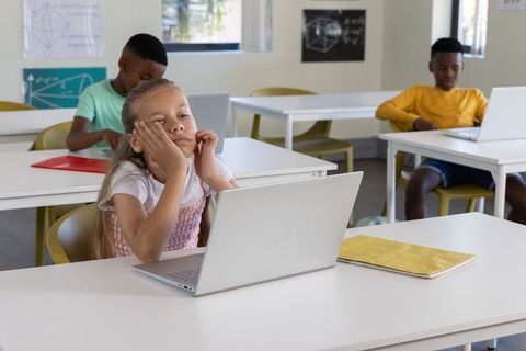 Elementary students using laptops in spacious classroom with bored girl daydreaming