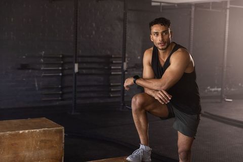 Male athlete pausing workout kneeling on plyo box wearing fitness tracker in urban gym