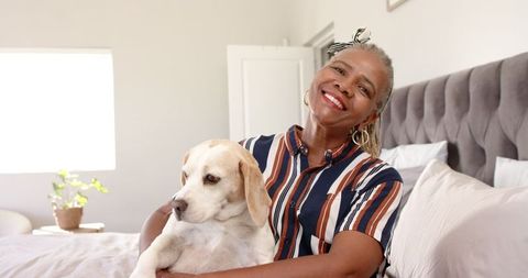 Senior Woman Joyfully Holding Dog on Bed in Bright Room