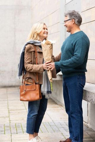 Senior couple exchanging bouquet and smiling on city walkway, romantic everyday moment