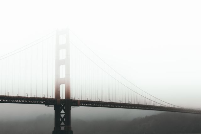 This image shows the Golden Gate Bridge in San Francisco partially shrouded by dense fog. The suspension bridge appears majestic yet mysterious, making it ideal for travel blogs, architectural articles, or promotional content related to San Francisco or California tourism. The fog adds a dramatic and visually intriguing element perfect for themes emphasizing mystery, nature, or weather phenomena.