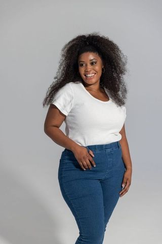 Smiling african american woman wearing white top and jeans standing on neutral background