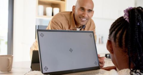 African American Father Helping Daughter with Laptop in Bright Modern Kitchen Homeschooling