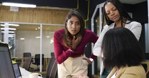Asian Indian woman collaborating with colleagues at laptop in modern office brainstorming