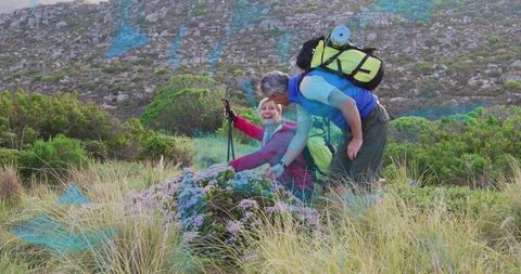 Senior couple hiking and resting on wildflower slope with backpacks and trekking poles