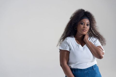 African american woman posing with curly hair wearing white ribbed top and denim jeans