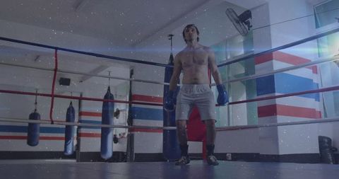 Shirtless boxer standing in ring wearing blue gloves preparing for intense training