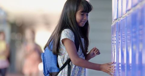 Young student opening school locker with blue backpack