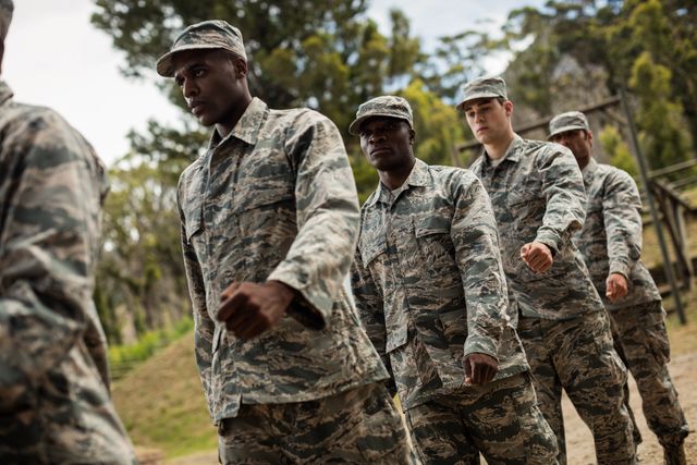 Group of military soldiers in camouflage uniforms marching in formation during a training session at boot camp. Ideal for use in articles about military training, teamwork, discipline, and physical fitness. Suitable for educational materials, recruitment campaigns, and motivational content.