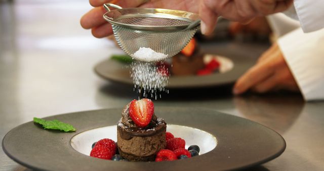 Hands of caucasian baker pouring sugar over chocolate cake in restaurant, copy space. Restaurant, food and drink, baking, dessert concept, unaltered.