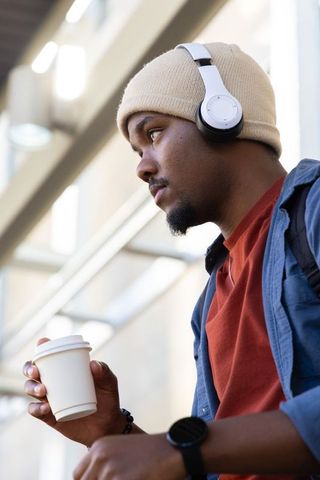 African American commuter listening to music holding coffee cup gazing in transit atrium