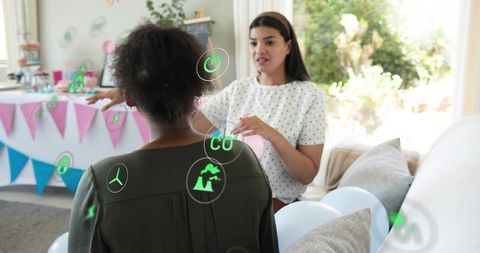 Women arranging pastel balloons with augmented reality party icons in living room