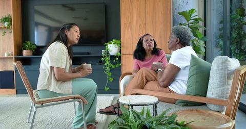 Mature women sharing coffee and conversation in cozy modern living room with indoor plants
