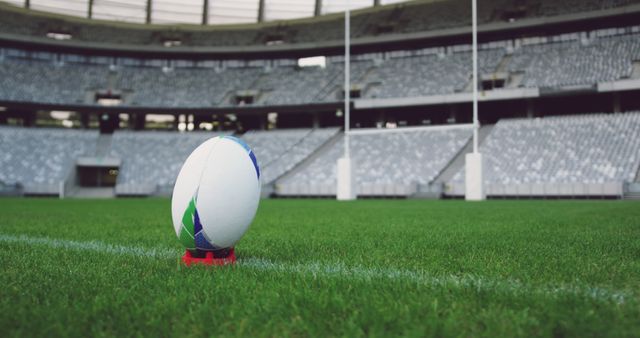 Rugby ball placed on a tee in an empty stadium, with goalposts ahead. Suitable for depicting sports preparations, anticipation of a game, or promotion of rugby events.