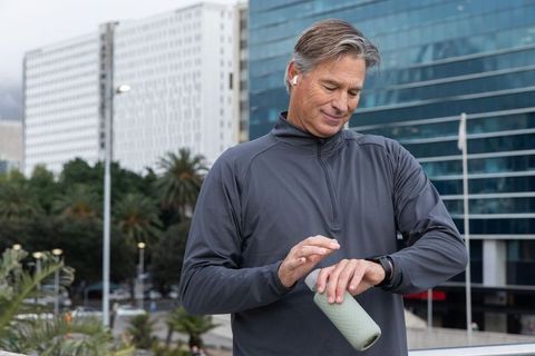 Middle-aged man checking smartwatch while holding reusable bottle on city fitness walk