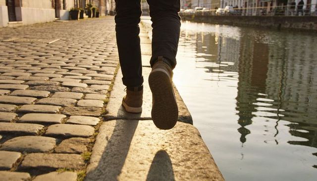 Balancing on quay edge walking along canal at golden hour cobblestone promenade