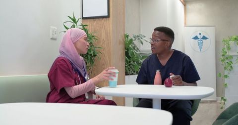 Diverse healthcare professionals chatting in clinic break room over coffee and snacks