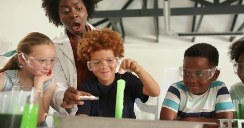 Diverse kids conducting foaming green chemistry experiment with teacher reacting excitedly