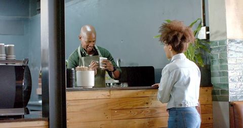 Barista writing order on takeaway cup while serving customer at wooden cafe counter