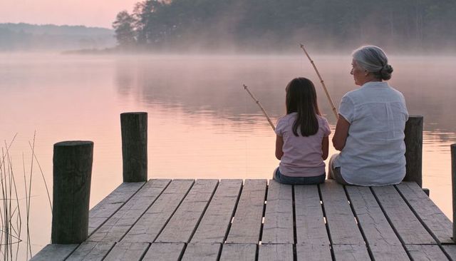 Grandmother and granddaughter fishing on misty lake dock at dawn, generational bonding