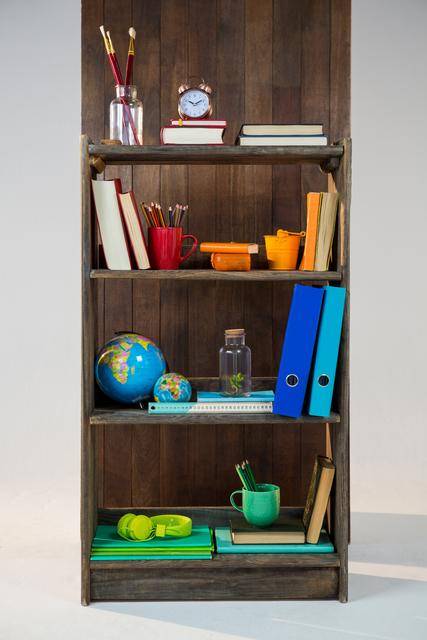 Wooden shelf neatly organized with various office and study supplies including books, a globe, a clock, binders, and colorful stationery. Ideal for illustrating concepts of organization, productivity, and workspace setup. Suitable for use in educational materials, office supply advertisements, and home office inspiration content.