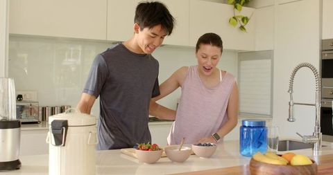 Young couple preparing healthy breakfast in bright modern kitchen, smiling and chatting