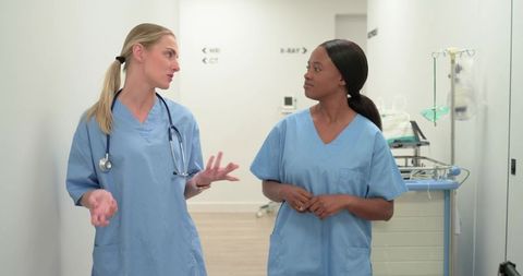Diverse nurses walking and discussing patient care in hospital corridor, showcasing teamwork