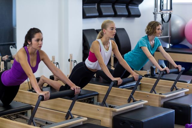 Women are engaging in a pilates workout using wunda chairs in a gym. This image is ideal for promoting fitness classes, gym memberships, pilates studios, and health and wellness programs. It highlights group exercise, strength training, and the use of specialized fitness equipment.