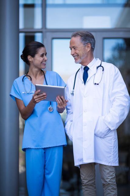 Doctor and nurse standing together, discussing patient information on a digital tablet. Both are smiling and appear to be collaborating effectively. Ideal for use in healthcare-related content, medical teamwork promotions, hospital brochures, and articles about modern medical practices.