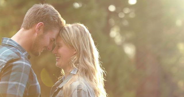 A young Caucasian couple shares a tender moment in a sunlit outdoor setting, with copy space. Their close proximity and affectionate expressions convey a sense of intimacy and romantic connection.