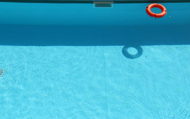 Top view of a swimming pool with a floating lifebuoy casting a shadow on the clear water. Useful for illustrating safety concepts, leisure activities, summer vacations, or relaxation by the poolside.