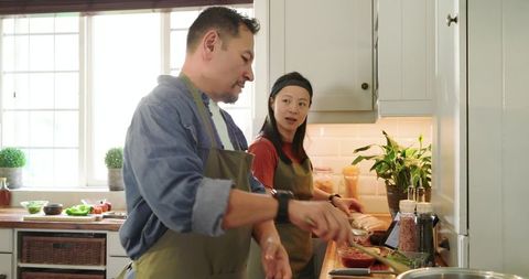 Asian Couple Cooking Together in Bright Kitchen Preparing Meal with Tablet and Spices