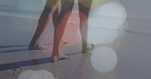 Couple walking on wet sand leaving footprints during golden hour with bokeh light flare