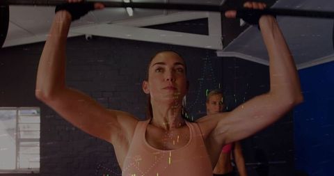 Midadult woman performing pull-up on bar during strength training with spotter in gym