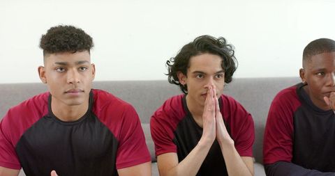 Three focused teammates watching match on couch wearing maroon black jerseys