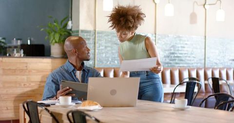 African american colleagues collaborating over laptop and papers in cafe workspace