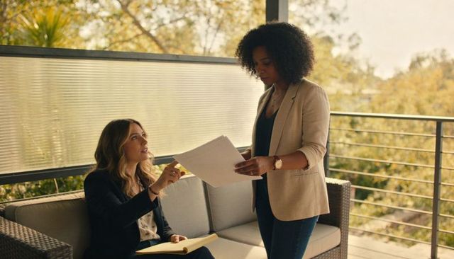 Two professional women reviewing documents on office balcony collaborating over contracts