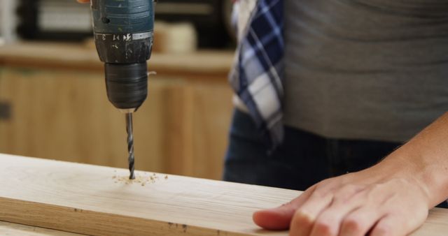 Focus on carpenter drilling a wooden plank in workshop