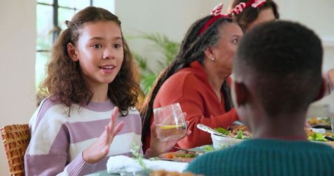 Multigenerational family sharing festive meal with girl holding glass at cozy home dining