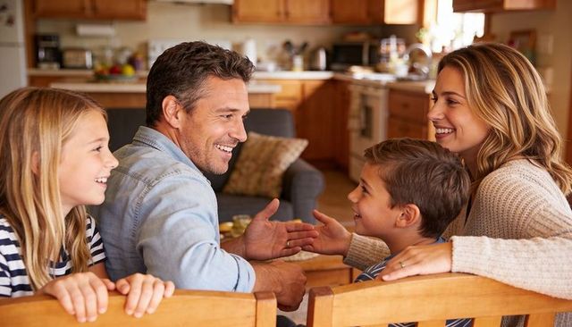 Family sharing laughter around kitchen table, parents and children enjoying together