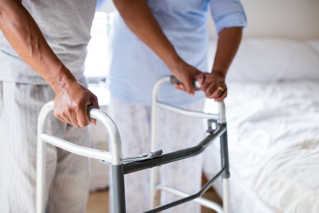 Mid-section of senior woman helping senior man to walk with walker at home