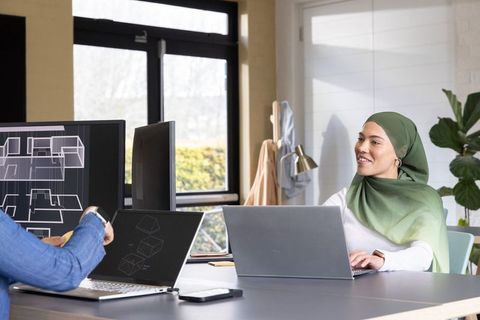 Woman wearing green hijab collaborating on cad designs with team using laptops and monitors