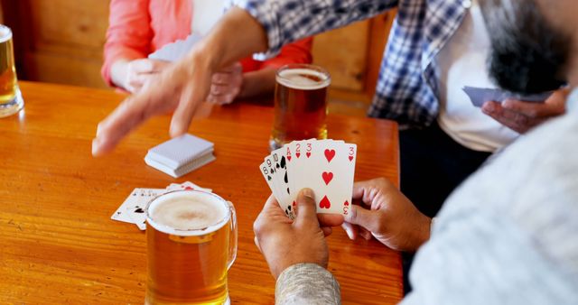 A group of people engage in a card game at a table, with drinks nearby, suggesting a casual social gathering. Cards in hand and a playful atmosphere indicate a moment of leisure and friendly competition.