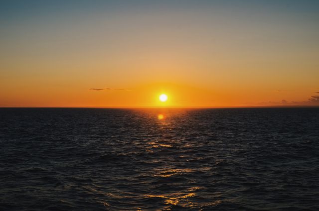 This image showcases a stunning sunset over a vast, calm ocean. The vibrant hues of orange and yellow blend seamlessly with the horizon, creating a peaceful and serene atmosphere. Ideal for nature-related content, travel platforms, or relaxation-themed projects. Can be used in blog posts, social media, website backgrounds, or inspirational themes promoting the beauty of nature and tranquility.