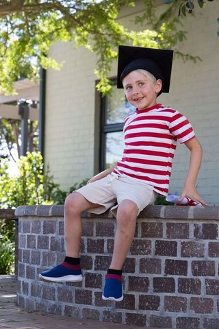 Young graduate boy in mortarboard holding diploma on brick wall celebrating milestone